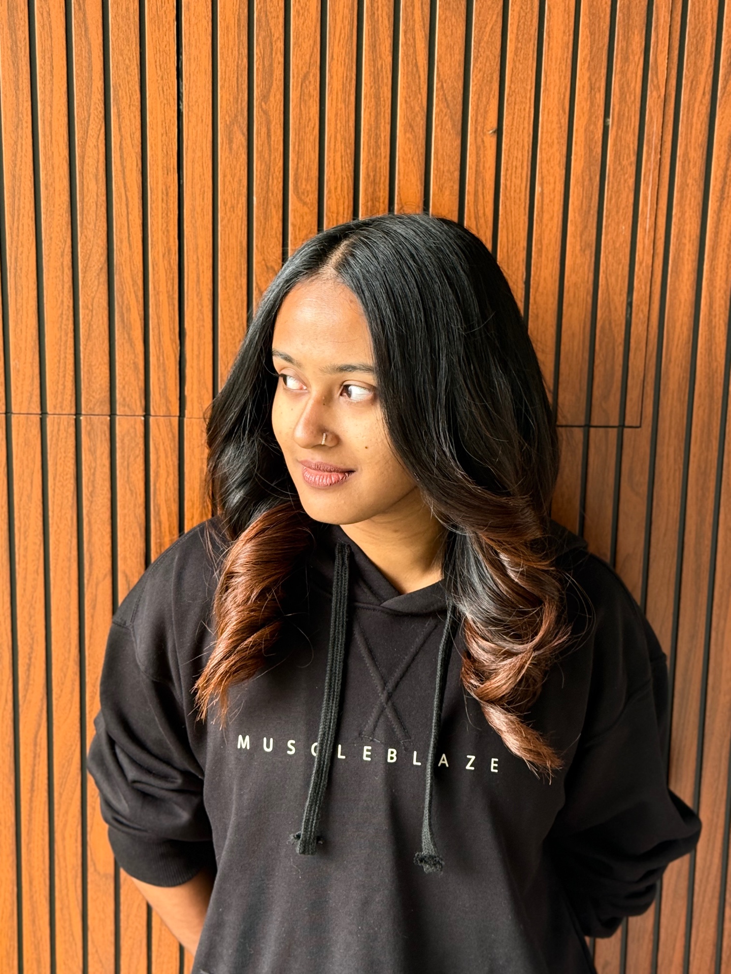 Aswathy in a black hoodie against a wooden wall